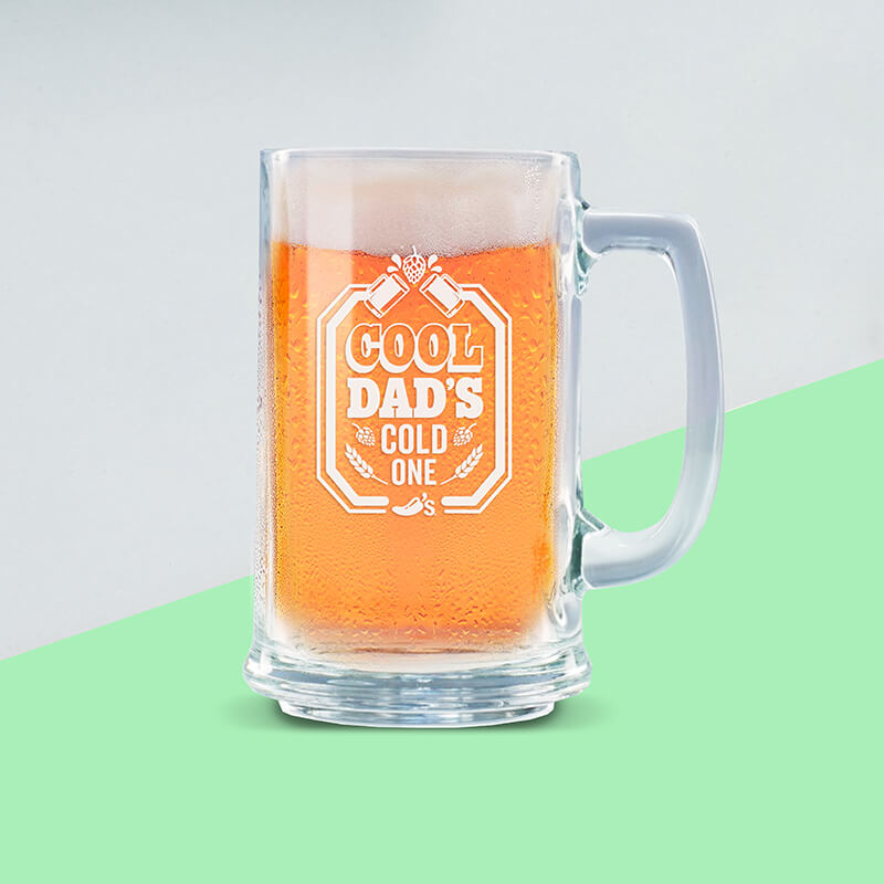 A glass beer stein, which reads "COOL DAD'S COLD ONE", is full of cool, crisp beer.